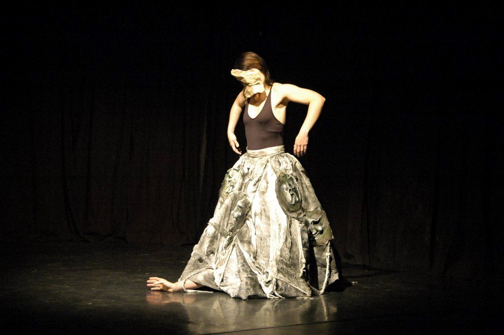 dancer moving with a heavy skirt made of masks with an arm poking from its bottom edge