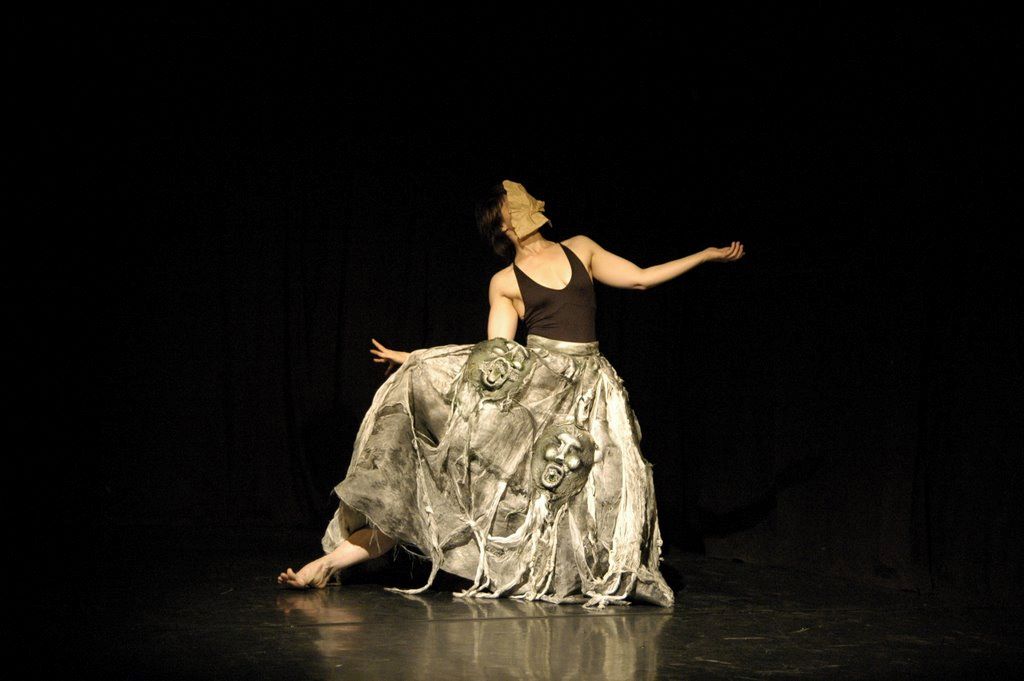 dancer moving with a heavy skirt made of masks with a leg poking from its bottom edge and an arm from its waistline 