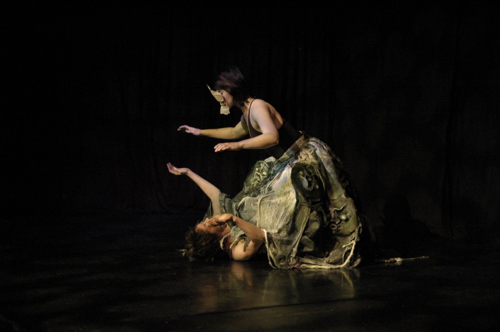 dancer moving with a heavy skirt made of masks with the torso and head of a second dancer poking from its bottom edge