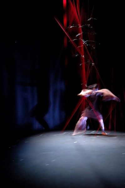 dancer moving in an installation of suspended red elastics attached floor to ceiling