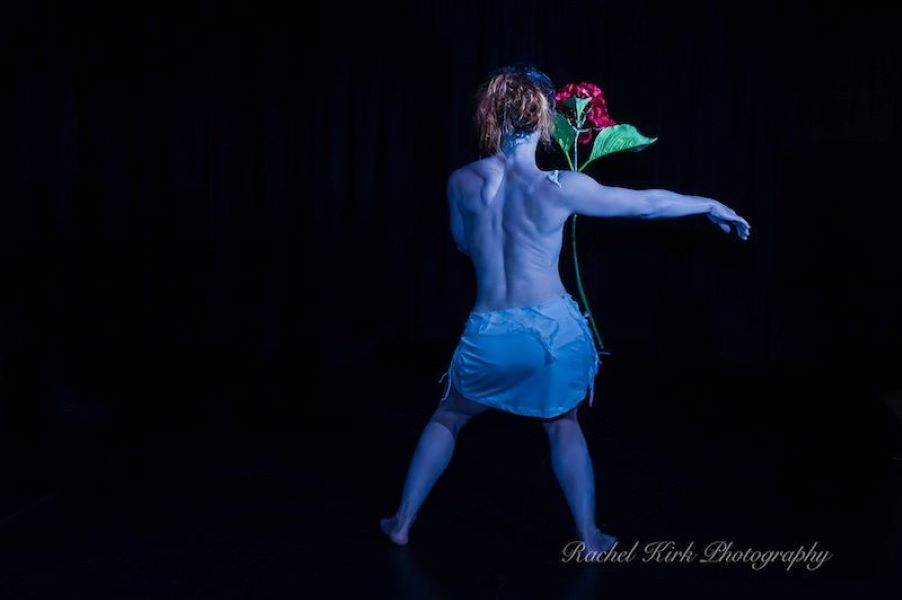female dancer's back moving around a floating red flower